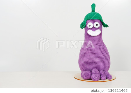 Unique knitted toy character in vibrant purple with green hat and cheerful expression, perfect for imaginative play and decorative purposes, featuring copy space for versatile use 136211465