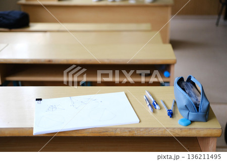Classroom desk with a blank sheet of paper, pens, and a pencil case, showcasing a learning environment with educational tools and materials for students Classroom desk with a blank sheet of paper, pens, and a pencil case, showcasing a learning environment with educational tools and materials for students 136211495