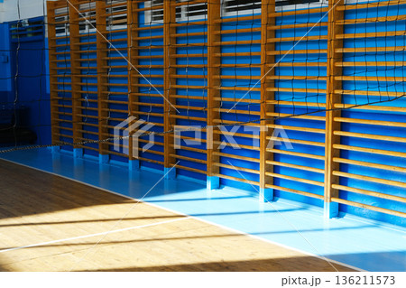 Interior view of a school gym featuring wooden climbing walls, blue walls, and polished wooden floors, creating an inviting atmosphere for sports education activities 136211573