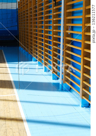 Interior of a sports hall featuring wooden climbing frames against a vibrant blue wall, with polished blue flooring reflecting natural light and creating a dynamic atmosphere 136211577