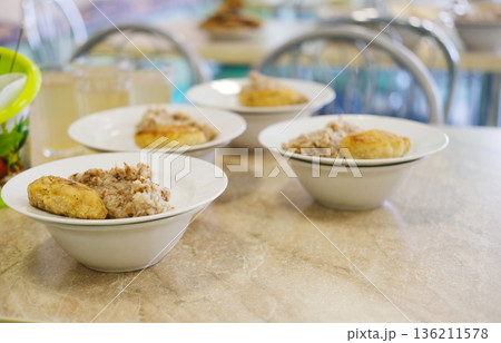 School cafeteria setting with bowls of hearty food, featuring a warm atmosphere and inviting textures, ideal for showcasing communal dining experiences and nutritious meals 136211578