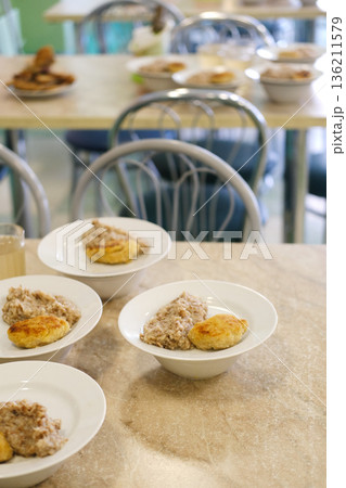 Bowls of hearty oatmeal and biscuits are arranged on a dining table in a cozy cafeteria setting, showcasing a warm and inviting breakfast atmosphere 136211579