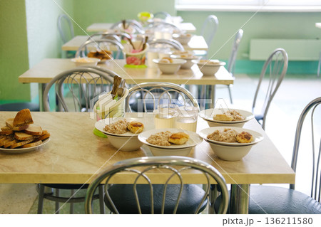 School cafeteria setting with tables arranged for lunch, featuring nutritious meals in bowls, promoting healthy eating habits for children and fostering well-being in educational environments 136211580