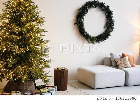 Christmas living room decor featuring a minimalist Scandinavian style with a beautifully lit tree, cozy sofa, and elegant wreath creating a warm festive atmosphere 136211606