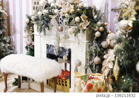 Elegant Christmas decorations adorn a cozy fireplace with a plush white bench, surrounded by festive greenery and shimmering ornaments, creating a warm holiday atmosphere Elegant Christmas decorations adorn a cozy fireplace with a plush white bench, surrounded by festive greenery and shimmering ornaments, creating a warm holiday atmosphere 136211632