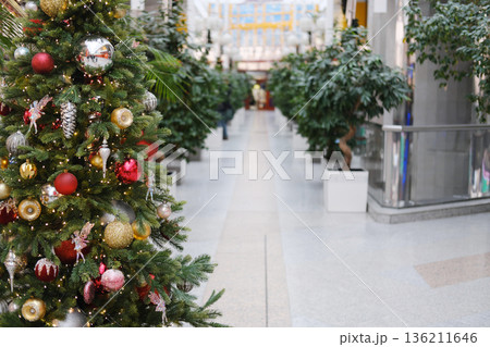Christmas tree adorned with colorful ornaments and twinkling lights stands in a festive public space, surrounded by lush greenery and a welcoming atmosphere for holiday travelers Christmas tree adorned with colorful ornaments and twinkling lights stands in a festive public space, surrounded by lush greenery and a welcoming atmosphere for holiday travelers 136211646