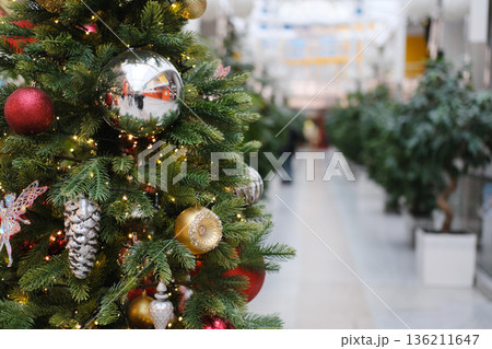 Christmas tree adorned with colorful ornaments and lights in a festive public space, surrounded by greenery, creating a warm holiday atmosphere with inviting decorations Christmas tree adorned with colorful ornaments and lights in a festive public space, surrounded by greenery, creating a warm holiday atmosphere with inviting decorations 136211647