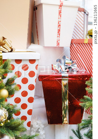 Colorful holiday gift boxes in various patterns, including polka dots and stripes, are arranged beside a decorated Christmas tree, creating a festive atmosphere for celebrations 136211665