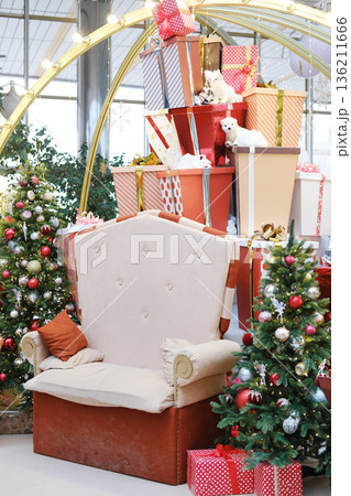 Festive Christmas decorations featuring a large plush chair surrounded by beautifully wrapped gifts and decorated trees in a vibrant public space creating a joyful holiday atmosphere 136211666