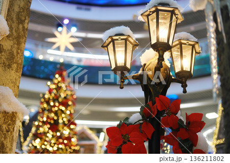 Christmas decorations featuring a charming fairytale town scene in a shopping mall, with illuminated street lamps, festive trees, and vibrant holiday colors creating a magical atmosphere 136211802