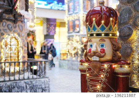 Colorful nutcracker decoration stands prominently in a festive shopping mall, surrounded by twinkling lights and holiday displays, creating a joyful Christmas atmosphere 136211807