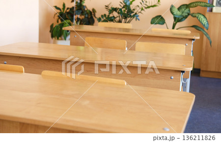 Classroom setting with wooden desks arranged neatly, surrounded by green plants, creating an inviting educational environment for students to learn and engage Classroom setting with wooden desks arranged neatly, surrounded by green plants, creating an inviting educational environment for students to learn and engage 136211826