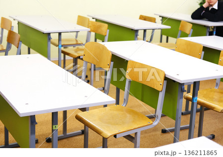 Classroom interior featuring empty wooden desks and chairs arranged in rows, with a soft color palette creating a calm learning environment, ideal for educational themes and concepts Classroom interior featuring empty wooden desks and chairs arranged in rows, with a soft color palette creating a calm learning environment, ideal for educational themes and concepts 136211865
