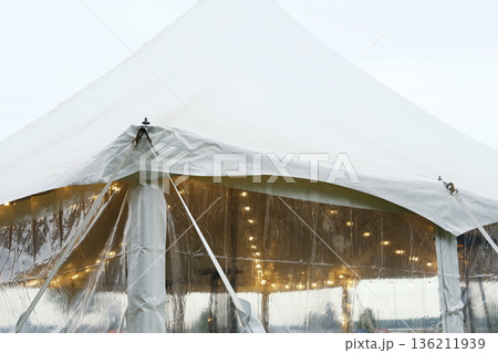 White tent secured with ropes and stakes, showcasing clear sides and warm lights inside, emphasizing stability and preparation for outdoor events and gatherings 136211939