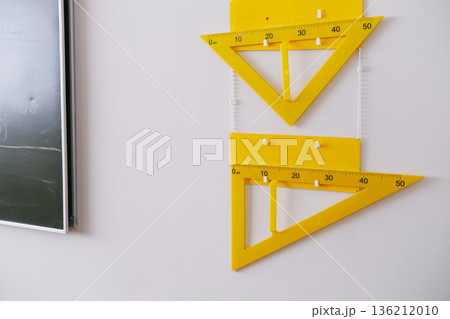 Yellow geometric tools including protractors and rulers are displayed on a classroom wall next to a chalkboard, emphasizing the importance of geometry in school education Yellow geometric tools including protractors and rulers are displayed on a classroom wall next to a chalkboard, emphasizing the importance of geometry in school education 136212010