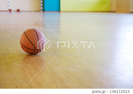 Basketball resting on polished wooden gym floor, surrounded by vibrant colored walls, representing sports education and physical activity in school environments Basketball resting on polished wooden gym floor, surrounded by vibrant colored walls, representing sports education and physical activity in school environments 136212023