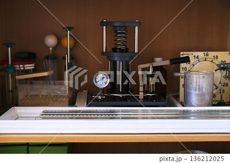 Laboratory equipment featuring a hydraulic press, pressure gauge, and measuring tools on a wooden shelf, showcasing precision instruments for scientific experimentation and analysis 136212025