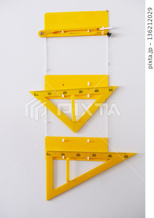 Yellow drafting tools including a protractor and triangle rulers arranged vertically on a white background, showcasing precision measurement and design elements in a creative workspace Yellow drafting tools including a protractor and triangle rulers arranged vertically on a white background, showcasing precision measurement and design elements in a creative workspace 136212029
