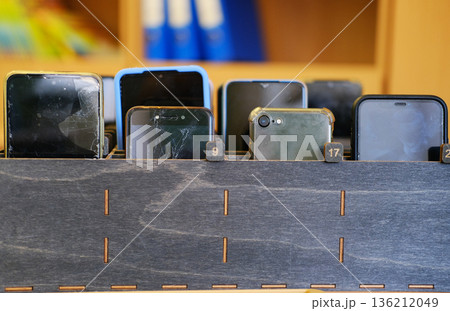 Collection of students' cell phones stored in a wooden box, showcasing various models and conditions, emphasizing the importance of device management in educational environments 136212049