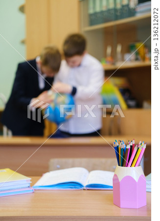Classroom scene featuring students engaged with a globe while a colorful pencil holder and open books create a vibrant educational atmosphere with copy space Classroom scene featuring students engaged with a globe while a colorful pencil holder and open books create a vibrant educational atmosphere with copy space 136212072