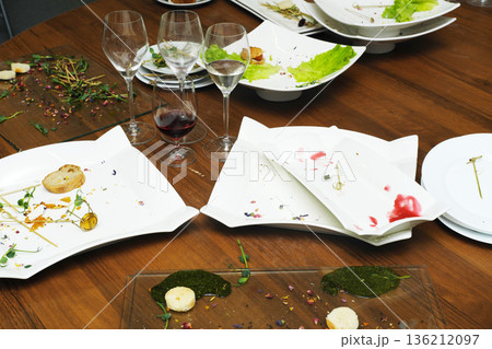 Elegant dining table with empty plates and wine glasses, showcasing remnants of a gourmet meal, surrounded by fresh greens and vibrant garnishes, creating a sophisticated culinary atmosphere Elegant dining table with empty plates and wine glasses, showcasing remnants of a gourmet meal, surrounded by fresh greens and vibrant garnishes, creating a sophisticated culinary atmosphere 136212097