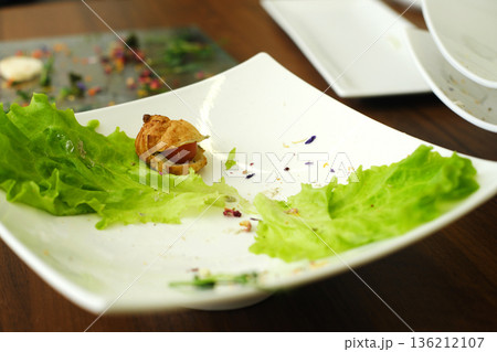 Empty white plate with remnants of food, featuring fresh green lettuce leaves and a small piece of pastry, showcasing a minimalistic dining experience and culinary presentation Empty white plate with remnants of food, featuring fresh green lettuce leaves and a small piece of pastry, showcasing a minimalistic dining experience and culinary presentation 136212107