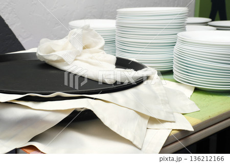 Catering setup featuring a black serving tray, neatly stacked white plates, and folded linens, creating an inviting atmosphere for food services at an event 136212166