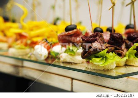 Colorful assortment of gourmet appetizers displayed on a glass platter, featuring skewers of meat, vegetables, and cheese, perfect for catering events and culinary presentations Colorful assortment of gourmet appetizers displayed on a glass platter, featuring skewers of meat, vegetables, and cheese, perfect for catering events and culinary presentations 136212187