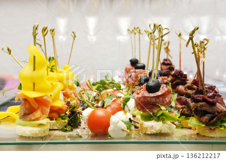 Colorful assortment of gourmet appetizers displayed elegantly on a glass platter, featuring vibrant ingredients and creative garnishes for catering and event services 136212217