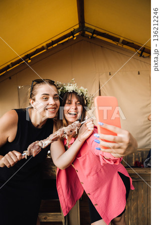 Friends taking selfie with kebab skewer at glamping tent barbecue Friends taking selfie with kebab skewer at glamping tent barbecue 136212246