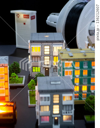Prototype building printed on 3D printer from melted plastic. 3D-printed building prototype. A house created on 3D printer with gray walls, gray roof, and illuminated windows and balconies. Prototype building printed on 3D printer from melted plastic. 3D-printed building prototype. A house created on 3D printer with gray walls, gray roof, and illuminated windows and balconies. 136212607