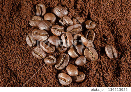 Top view of scattered coffee beans on a background of ground coffee Top view of scattered coffee beans on a background of ground coffee 136213923