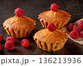 Freshly baked lemon muffins accompanied by juicy raspberries on a rustic kitchen table 136213936