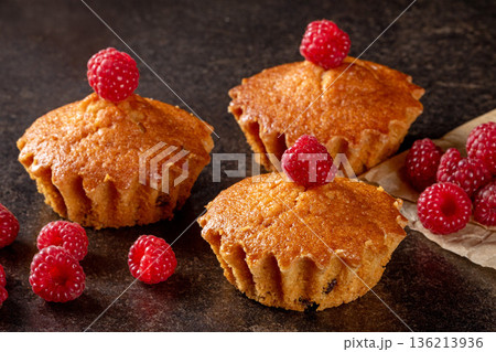 Freshly baked lemon muffins accompanied by juicy raspberries on a rustic kitchen table Freshly baked lemon muffins accompanied by juicy raspberries on a rustic kitchen table 136213936