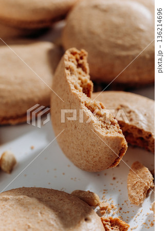 Bitten peanut macaron closeup with crumbs on white plate, shallow depth of field Bitten peanut macaron closeup with crumbs on white plate, shallow depth of field 136214696