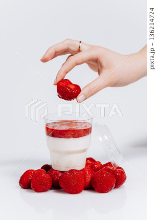 Hand placing strawberry on panna cotta in cup with berries on white background Hand placing strawberry on panna cotta in cup with berries on white background 136214724