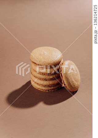 Beige macarons stacked on brown background, minimal French dessert 136214725