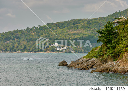 Thailand's coast on a sunny day, villas and hotels among palm trees on a hill, people on a jet ski, a yacht off the coast 136215389