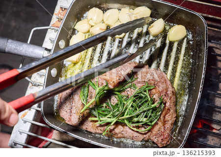barbecue party, close-up image of grilling steaks, the meat is stewed in butter with garlic and thyme, spiking pieces of meat on the grill, various vegetables, lots of smoke 136215393