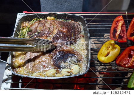 barbecue party, close-up image of grilling steaks, the meat is stewed in butter with garlic and thyme, spiking pieces of meat on the grill, various vegetables, lots of smoke barbecue party, close-up image of grilling steaks, the meat is stewed in butter with garlic and thyme, spiking pieces of meat on the grill, various vegetables, lots of smoke 136215471