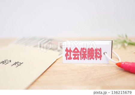 給料袋と紙幣。社会保険料を示すカード。 給料袋と紙幣。社会保険料を示すカード。 136215679
