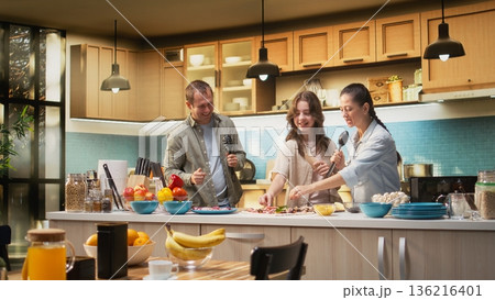 African American family enjoying silly karaoke session for pizza day in the kitchen, singing with utensils and doing goofy dance moves together. Weekend activity and cooking time. 136216401