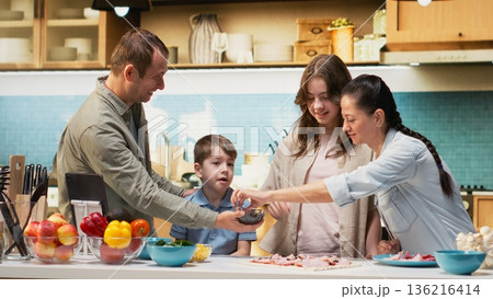 Adorable family cooking at home and enjoying pizza day together. Children and parents adding fresh ingredients and creating delicious homemade pizza while sharing laughter. Adorable family cooking at home and enjoying pizza day together. Children and parents adding fresh ingredients and creating delicious homemade pizza while sharing laughter. 136216414