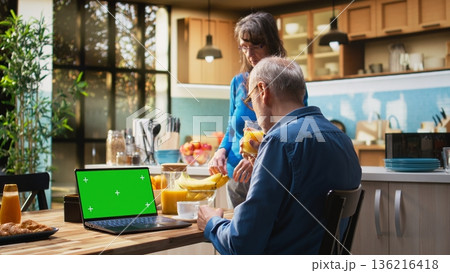 Chroma key laptop with retired man checking display at the table in rustic kitchen, relaxed senior people spending their cozy lifestyle at home. Serving coffee and pastry. Camera A. Chroma key laptop with retired man checking display at the table in rustic kitchen, relaxed senior people spending their cozy lifestyle at home. Serving coffee and pastry. Camera A. 136216418