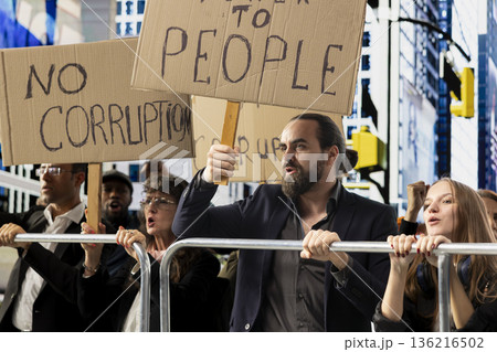 Multiethnic people protesting together during strike and public march against corruption, holding posters and banners with warning messages about justice in anti-corruption movement. Multiethnic people protesting together during strike and public march against corruption, holding posters and banners with warning messages about justice in anti-corruption movement. 136216502