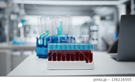 Close up of small glass flasks containing red blood samples on laboratory workbench. Sanguine fluid specimens prepared for clinical diagnostic testing in sterile environment Close up of small glass flasks containing red blood samples on laboratory workbench. Sanguine fluid specimens prepared for clinical diagnostic testing in sterile environment 136216505