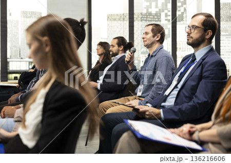 Male CEO in attendance asking questions during conference discussion, engaging in professional debate and listening to speech. Group of white collar workers attend international summit. Male CEO in attendance asking questions during conference discussion, engaging in professional debate and listening to speech. Group of white collar workers attend international summit. 136216606