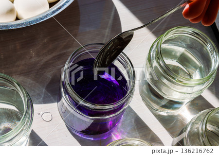 Top view of a glass jar filled with water colored with deep purple food dye being stirred with the spoon on a sunlit table 136216762