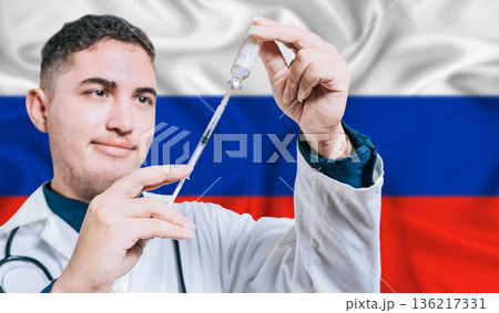 Doctor holding syringe on Russia flag background. Medical professional holding syringe with Russian flag in the background Doctor holding syringe on Russia flag background. Medical professional holding syringe with Russian flag in the background 136217331