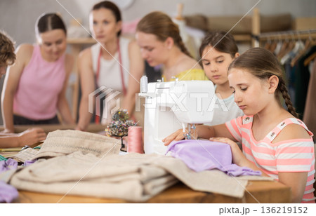 Tween schoolgirl stitching fabric on machine in school tailoring workshop 136219152